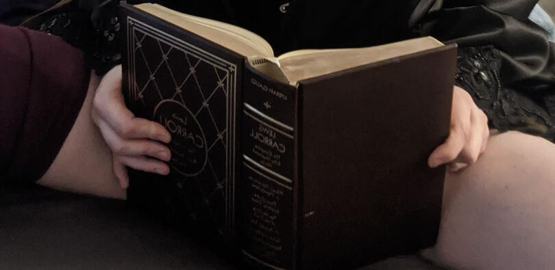 A leatherbound copy of Lewis Carroll's books placed suggestively in front of open legs.